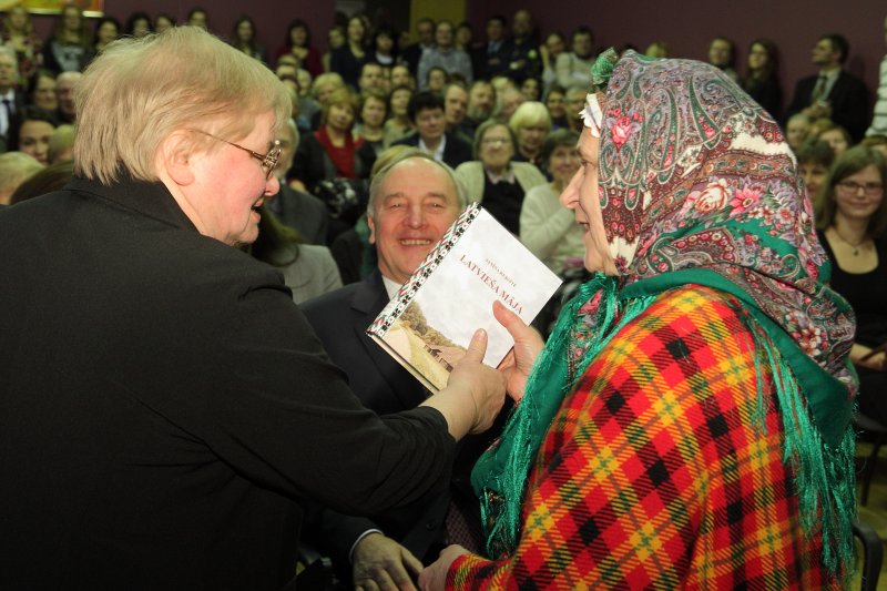 Sarīkojums «Treji vārti» Latvijas Universitātes Humanitāro zinātņu fakultātē. LU Humanitāro zinātņu fakultātes profesore, LR Saeimas deputāte Janīna Kursīte-Pakule (pa kreisi)
dāvina savu grāmatu 'Latvieša māja' etnogrāfiskā ansambļa 'Suitu sievas' vadītājai Ilgai Leimanei.